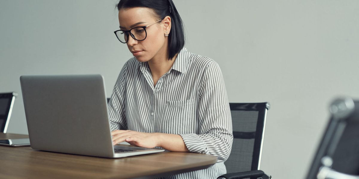 Young businesswoman in eyeglasses concentrating on her online work she sitting at the table and typing on laptop computer